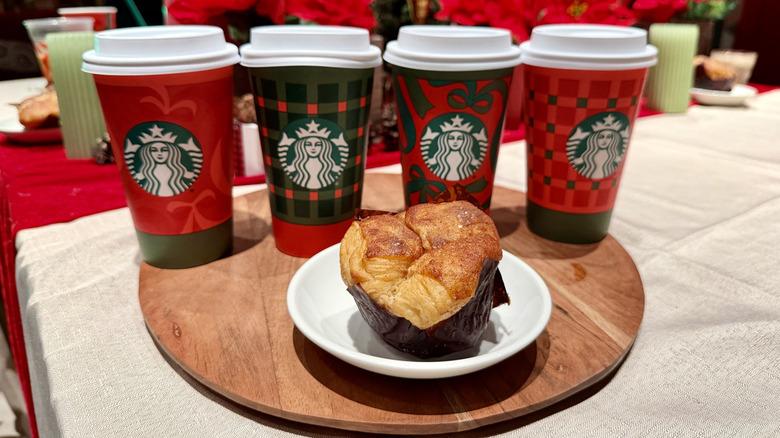 A Cinnamon Pull-Apart Bread from Starbucks on a plate on top of a wooden platter with Christmas-themed Starbucks coffee cups behind