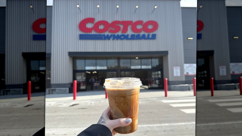 A hand holding a drink in front of a Costco store