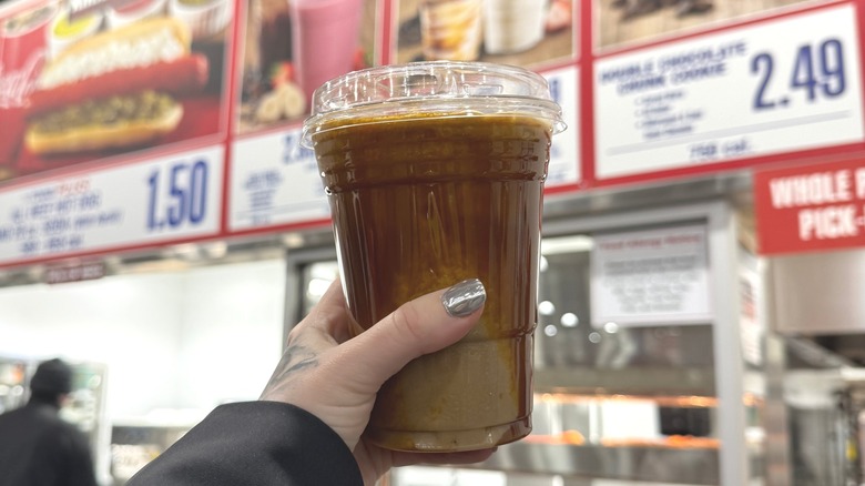 A hand holding a drink in front of Costco food court signs