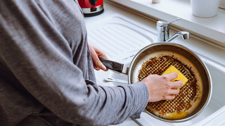 Woman scrubbing burnt pan in sink