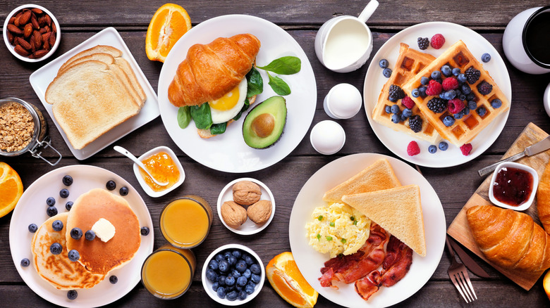A top-down view of several different American breakfast staples like waffles, toast, and pancakes on white plates