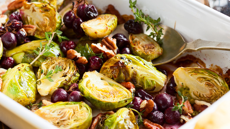 roasted brussels sprouts with grapes, thyme, and walnuts in baking dish with spoon