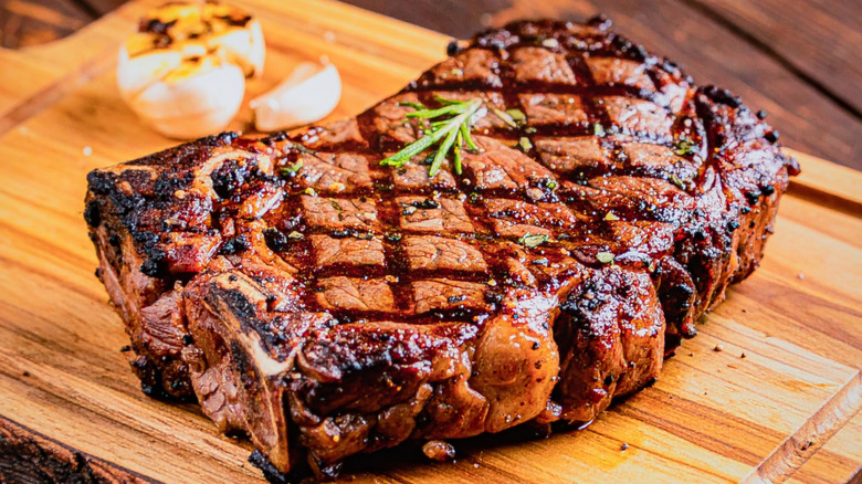 Cooked ribeye steak on wooden cutting board with garlic and rosemary.