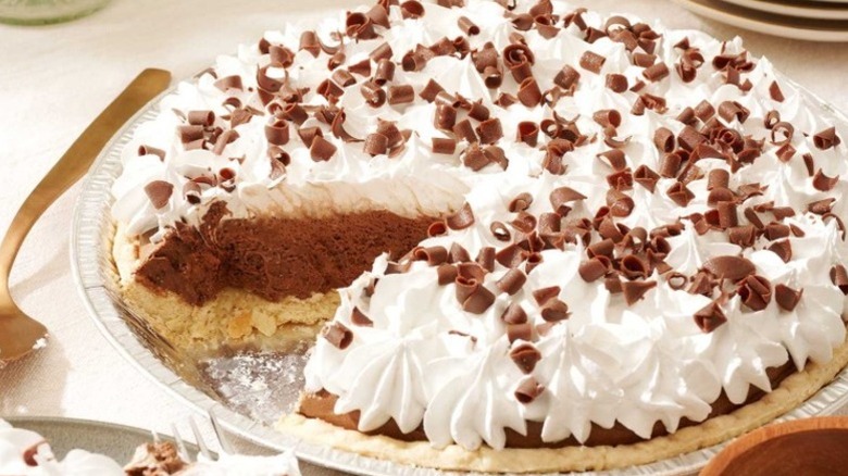 french silk pie topped with whipped cream and chocolate shavings, with one slice missing