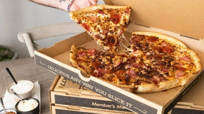 hand reaching for a slice of pepperoni pizza in a box