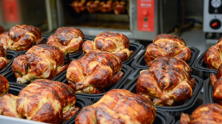 Rotisserie chickens in black plastic containers at a grocery store.