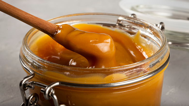 Dulce de leche in glass jar with wooden spoon