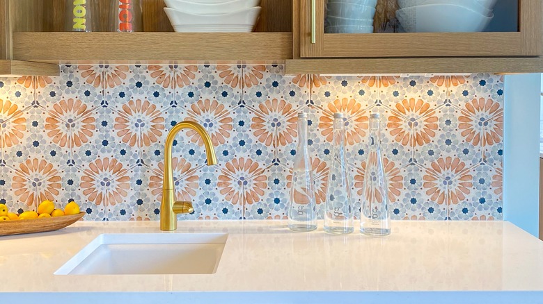 A colorful, patterned vinyl backsplash behind a white surface and gold faucet.