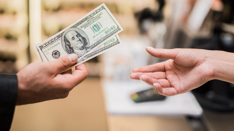 Hand giving two $100 bills to another hand