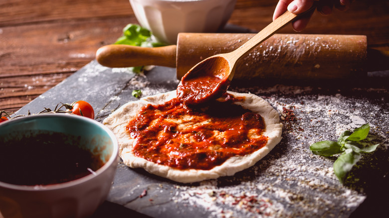 Spooning pizza sauce on dough