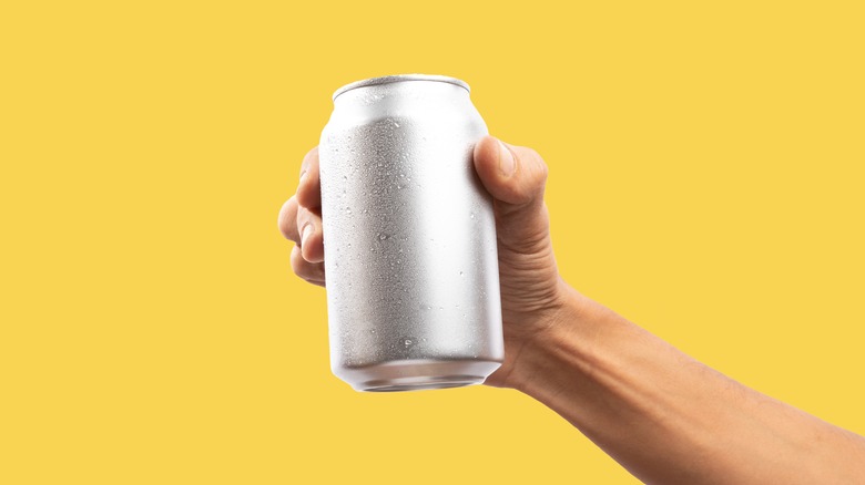 Hand holding up soda can on yellow background