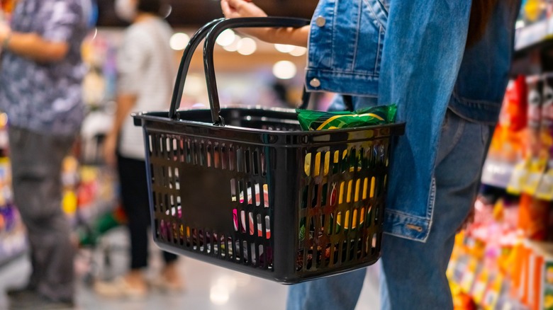 A woman holds a basket while shopping in a supermarket