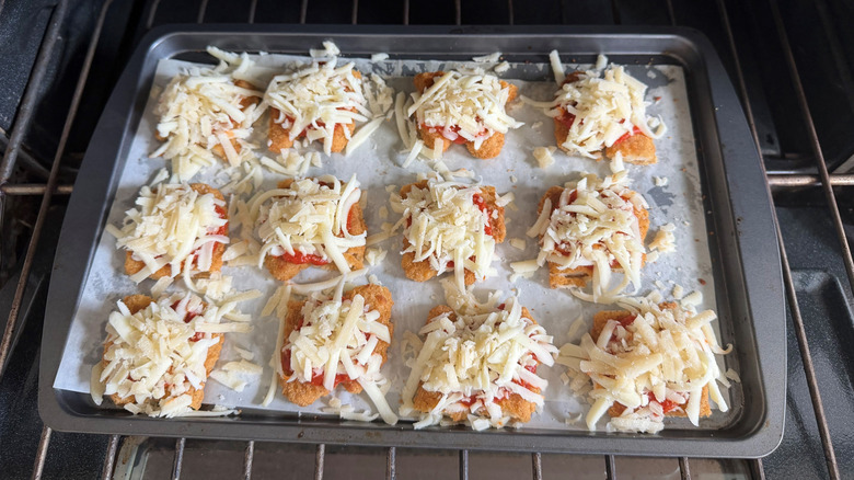 Chicken strips topped with marinara and mozzarella on baking sheet
