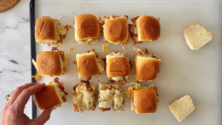 Hand placing top bun onto chicken parmesan slider