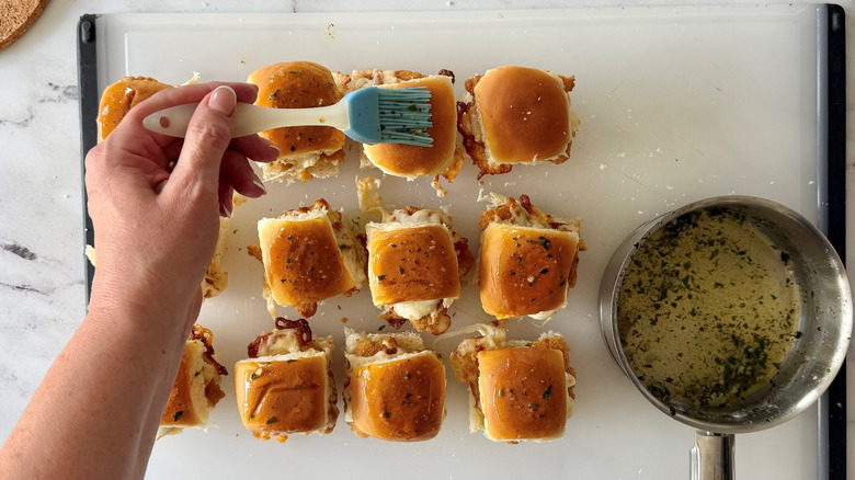 Hand brushing chicken parmesan sliders with garlic butter