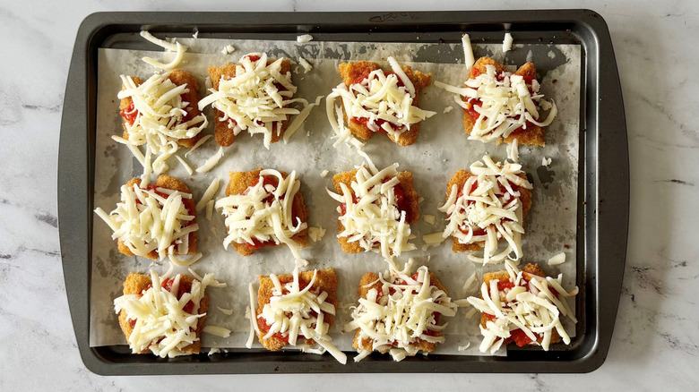 Portions of chicken strips topped with marinara and mozzarella on baking sheet