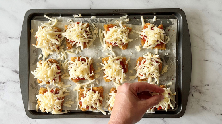 Hand placing cheese onto chicken parm slider base on baking sheet