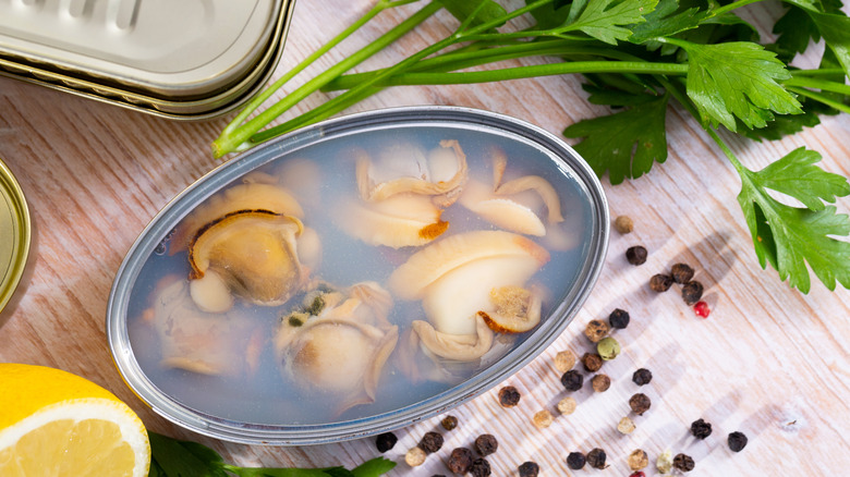 Canned clams next to whole peppercorns and parsley sprig