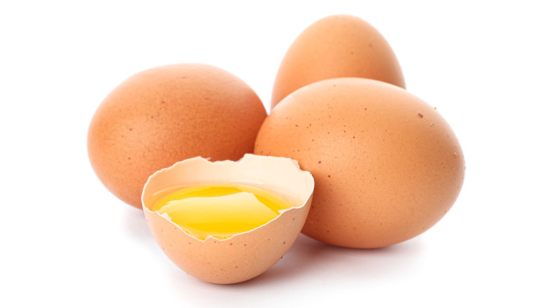 Three whole brown eggs, one cracked in half, exposed yolk