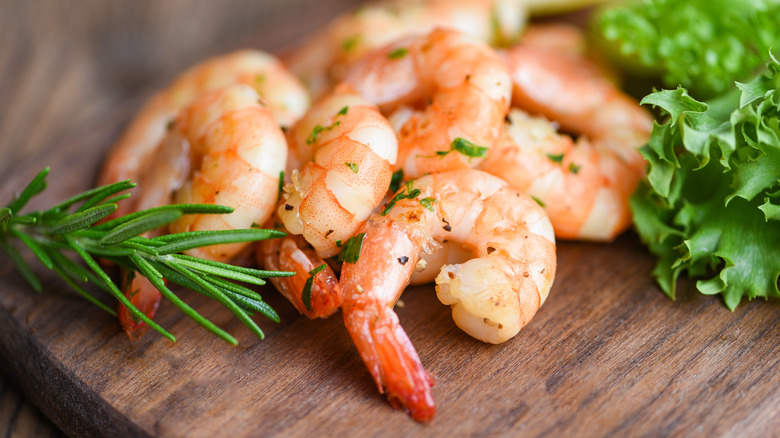 Cooked pink shrimp on a cutting board with herbs
