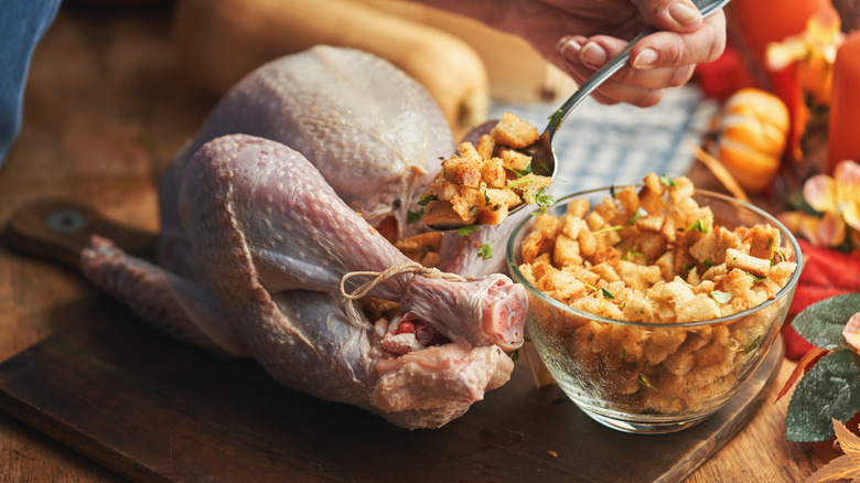 Hand spooning stuffing inside raw turkey