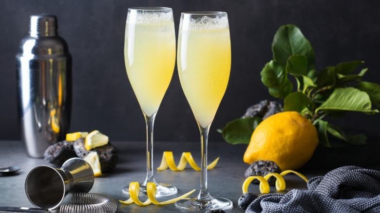 Two French 75 cocktails surrounded by lemons, lemon zest garnishes, and bar paraphernalia