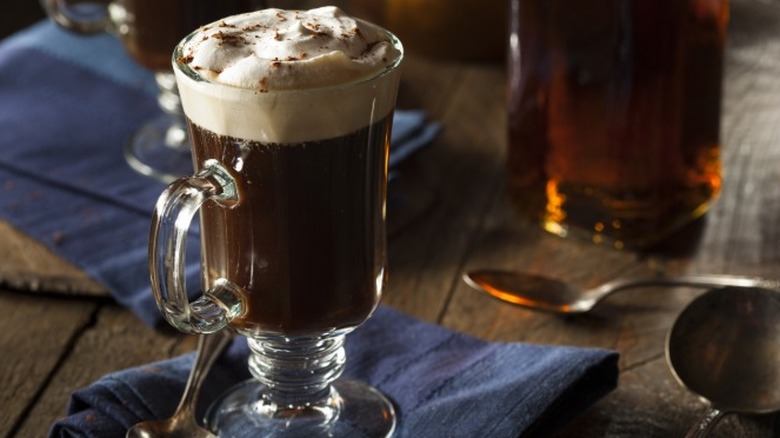 An Irish coffee cocktail in a clear glass mug topped with whipped cream