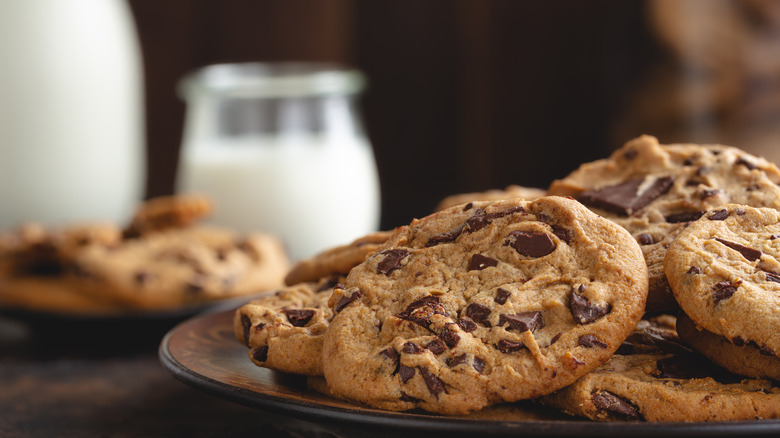 A close-up of a plate of chocolate chip cookies with a glass of milk in the background