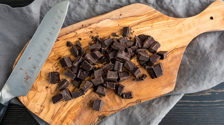Chopped up chocolate next to a knife on a rustic wooden cutting board