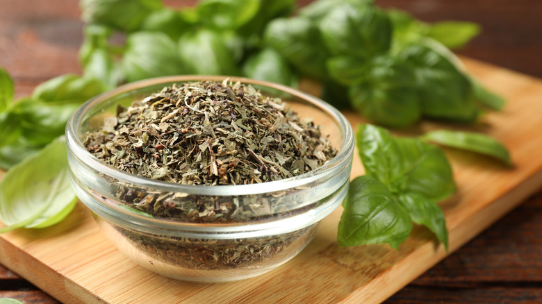 A small glass bowl of dried basil, with fresh basil in background