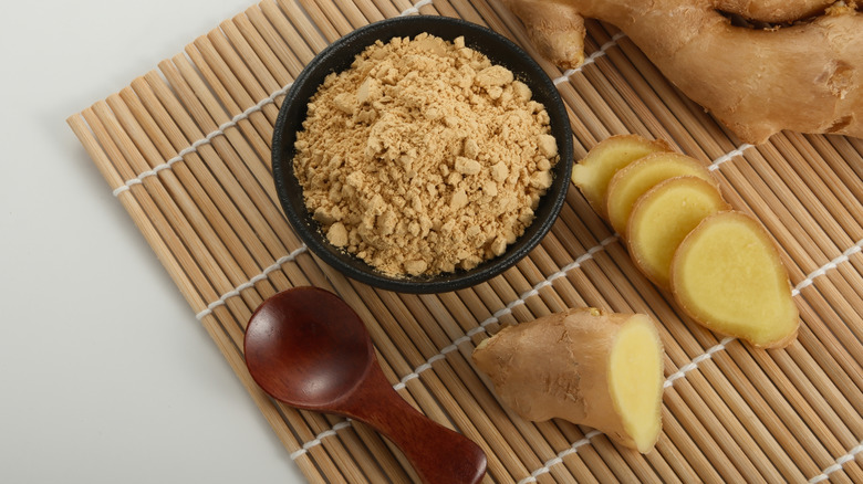 A small black bowl of powdered ginger next to fresh ginger root slices