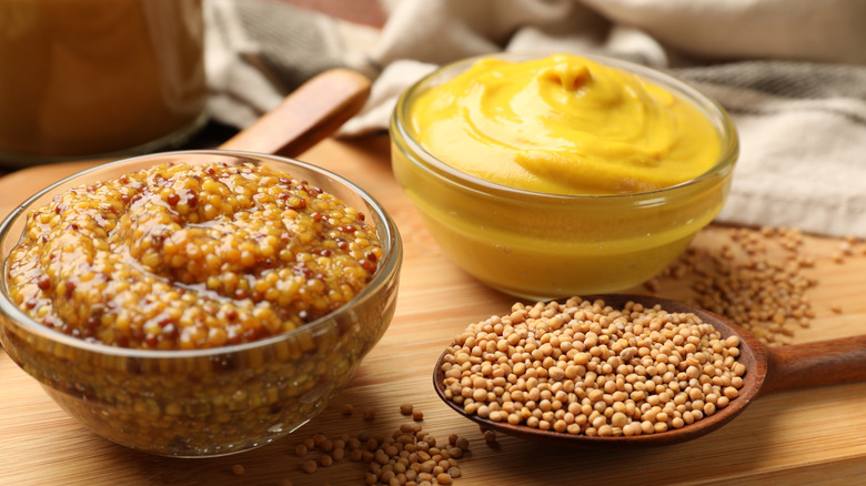 Small bowls of yellow and Dijon mustard next to each other, with mustard seeds