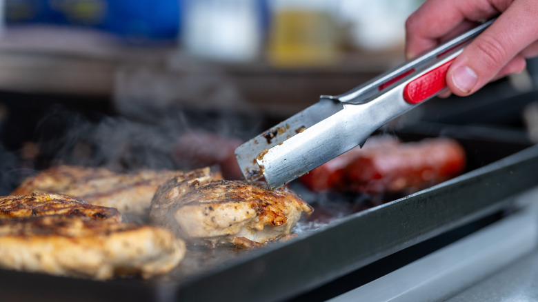 Tongs flipping chicken on a flattop griddle
