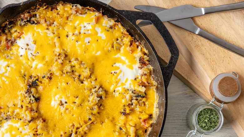 Hash browns covered with cheese in a skillet with small jars of herbs next to it