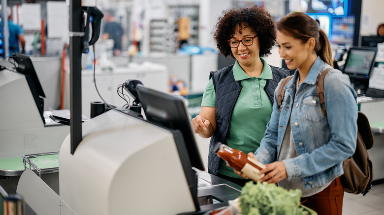 cashier helps a customer use self-checkout lane