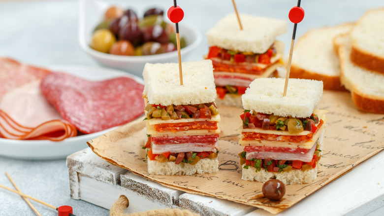 Three mini muffulettas and ingredients on a wooden platter