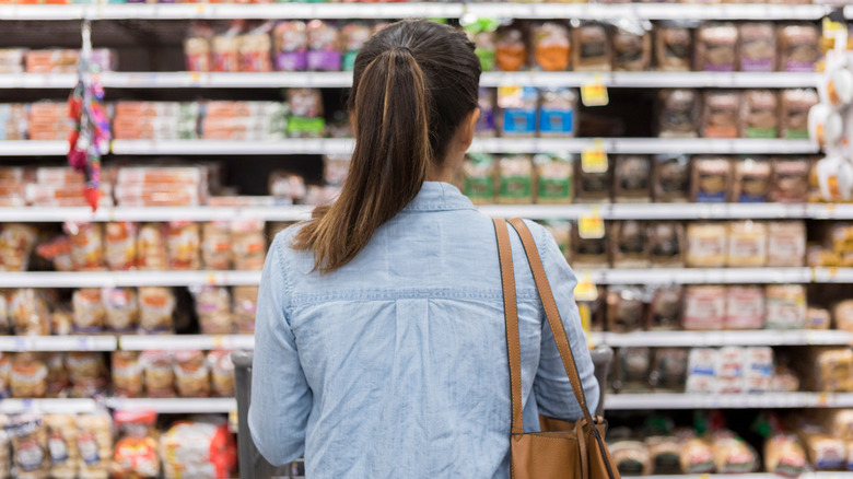 A view of a woman from behind while she contemplates a row of grocery shelves