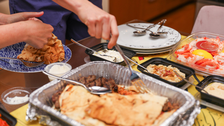 Several people scoop food onto plates from a potluck table