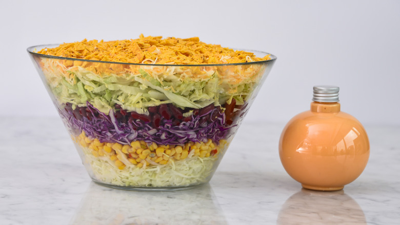 A seven-layer salad sits next to a bottle of dressing