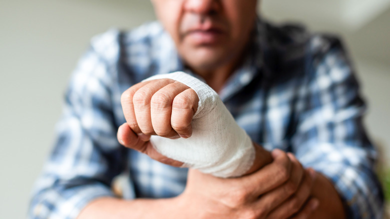 person in plaid shirt holding their bandaged hand