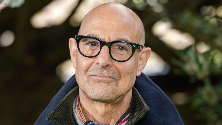 Stanley Tucci wearing several layers and glasses outside.