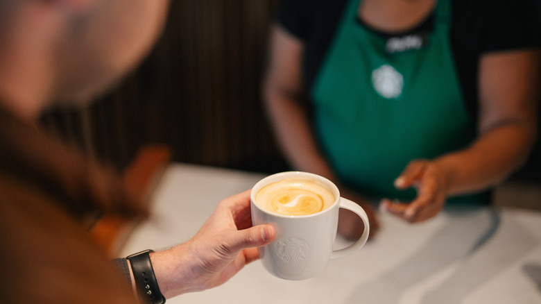 Person accepting coffee in a white mug from a Starbucks barista