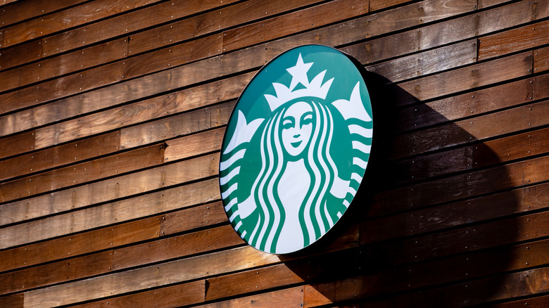 Round green Starbucks logo on a brown wooden wall, facing the sun
