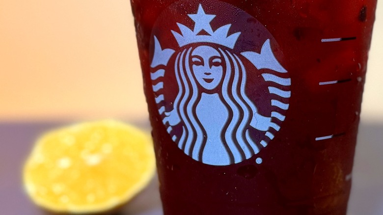 Close-up of Starbucks logo on cup, with a slice of lemon in the background.