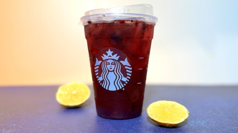 Deep red Starbucks refresher in branded plastic cup, with lemon slices.
