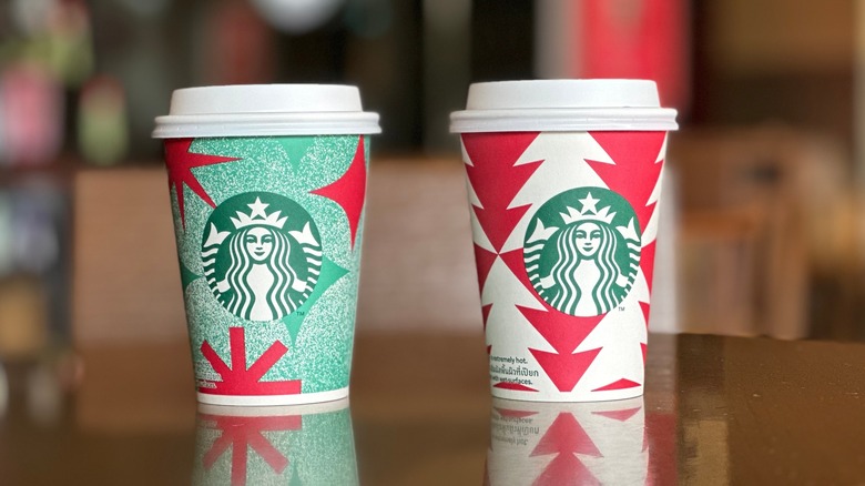 two holiday themed Starbucks cups sit on a table