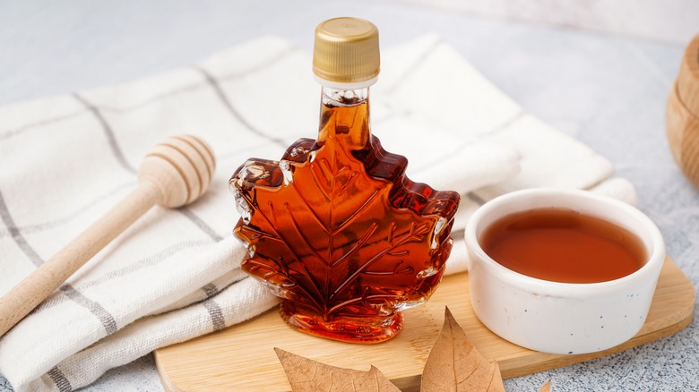 Maple syrup in leaf shaped bottle next to a bowl filled with syrup