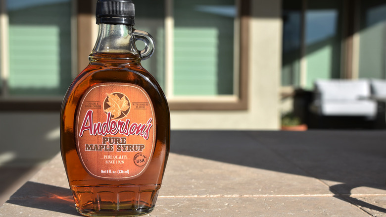 A bottle of Anderson's labeled, "pure maple syrup" on an outdoor table