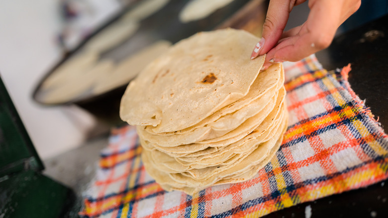 A stack of fresh flour tortillas sits on a kitchen towel on the counter.