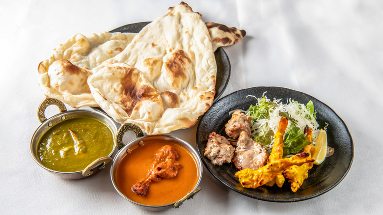 Two types of curries, a plate full of kebabs, and naan, all of a white table